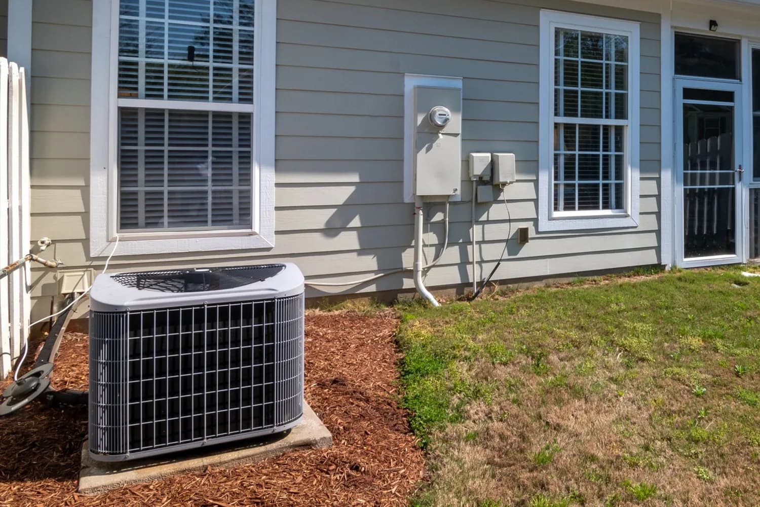 Clean residential air conditioning condenser on a concrete pad beside a home in bright sunlight